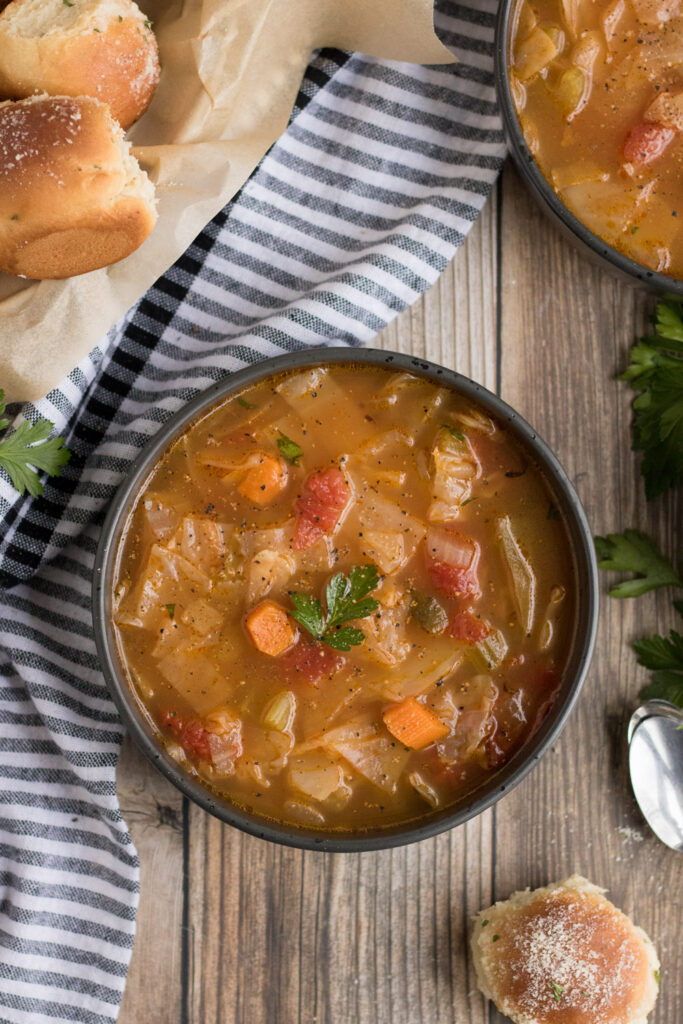 vegan cabbage soup- soup in a black bowl with some rolls around it