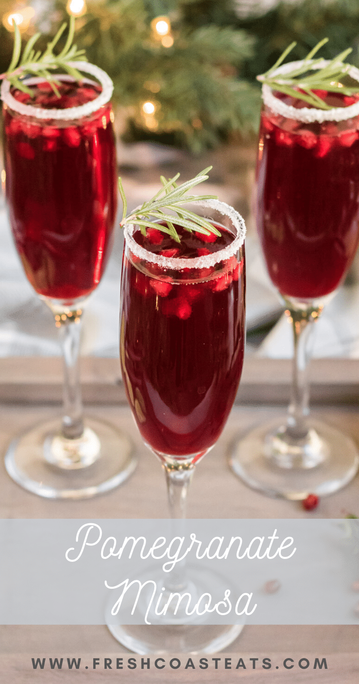 Pomegranate Mimosa- three champage glasses with pomegranate mimosa's. They are garnished with sugared rims and a sprig of rosemary.