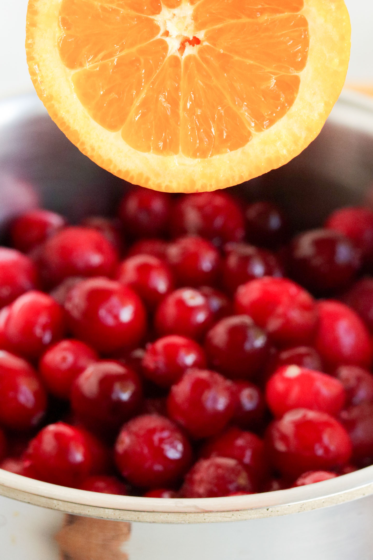 Cranberry Orange Sauce, a close up shot of an orange being squeezed over gresh cranberries. 