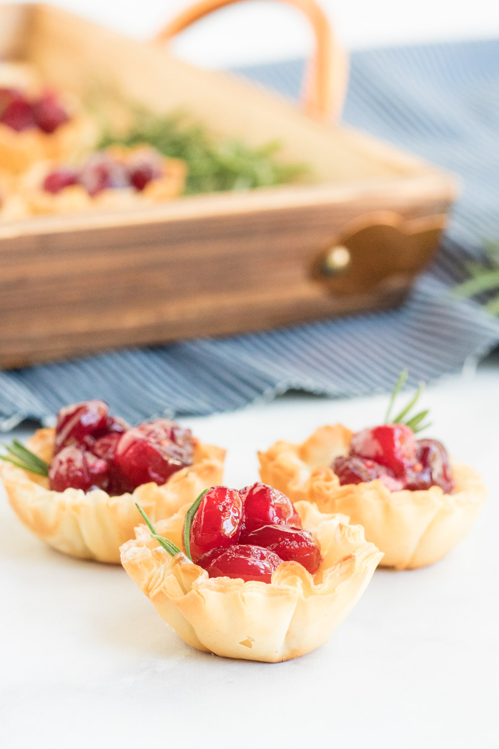 Cranberry Brie Bites- picture of a phyllo shell filled with brie cheese and cranberry and a sprig of rosemary