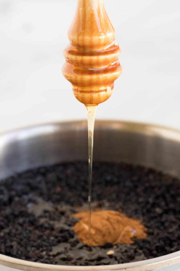 elderberry syrup recipe, honey is being drizzled over elderberries