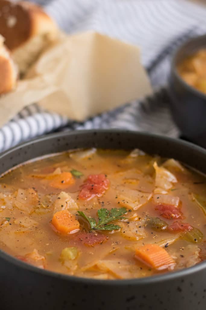 A bowl of vegan cabbage soup in a black bowl with bread in the background