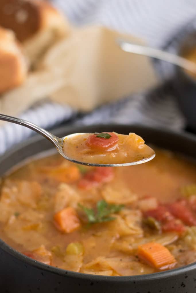 Vegan Cabbage Soup- a spoonful of delicious vegan cabbage soup hovering over a black bowl.