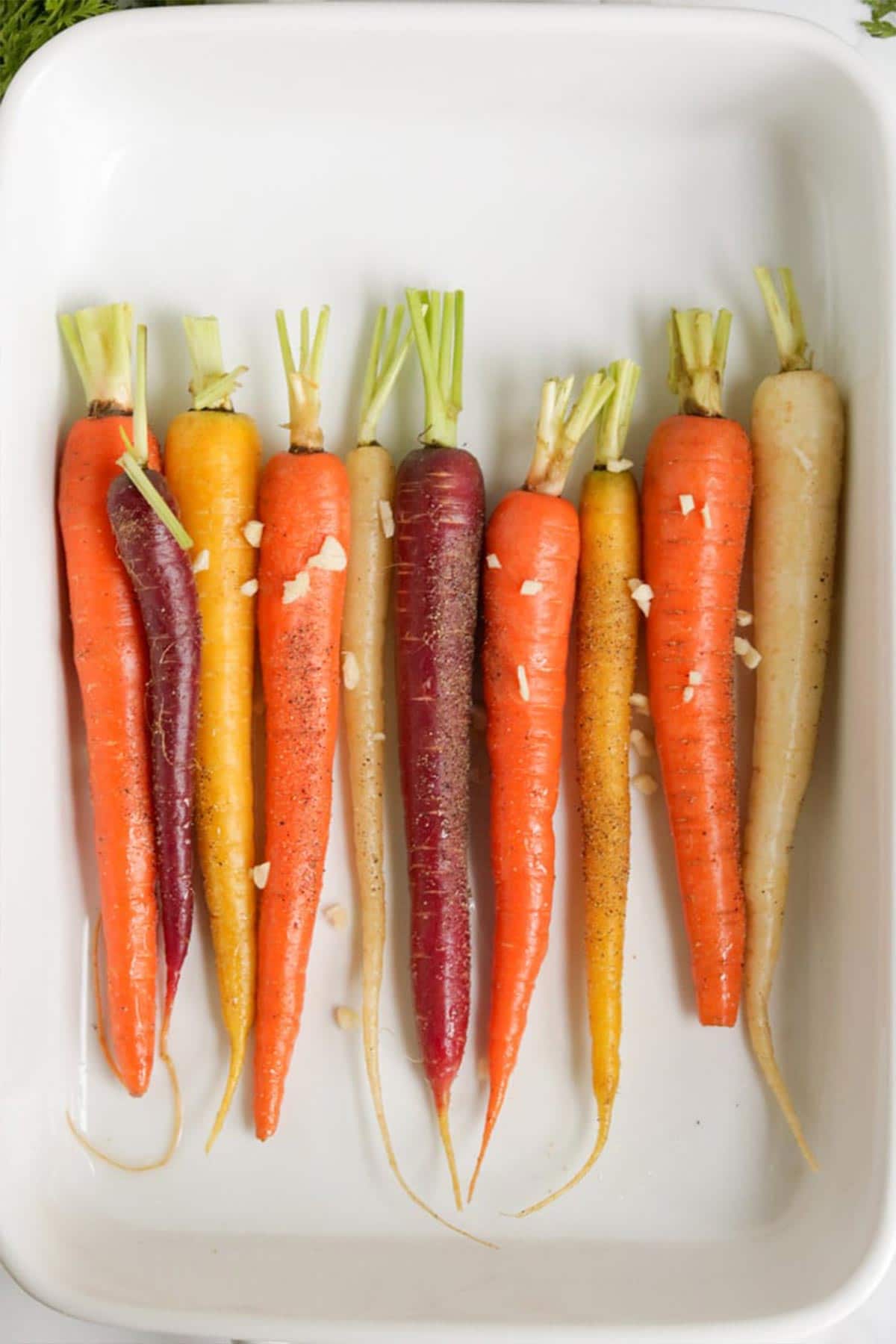 Whole Roasted Rainbow Carrots: Raw carrots placed in a single layer in a baking dish in preparation for baking. 