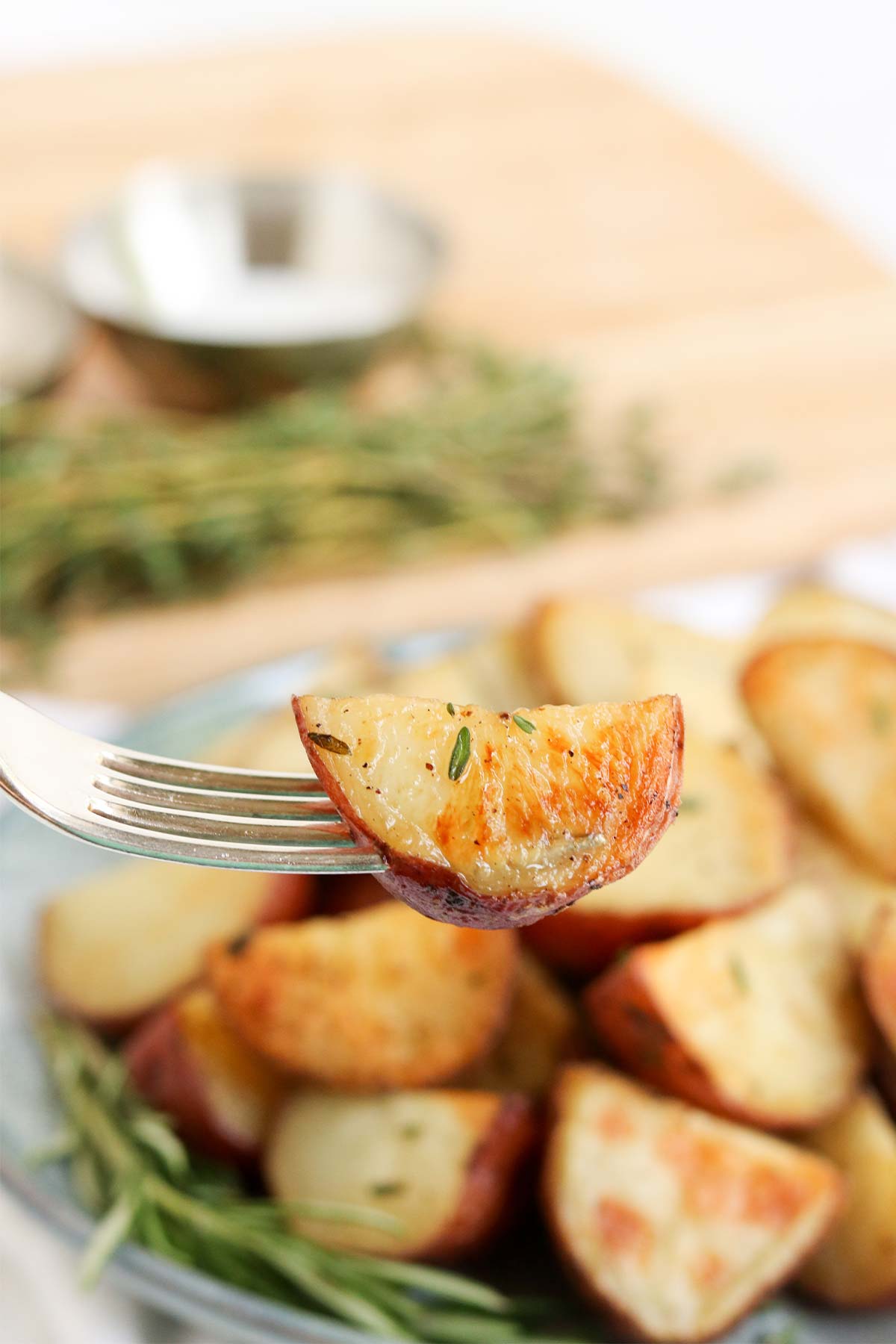 Roasted Rosemary Potatoes- a picture of a plate with roasted rosemary potatoes on them with rosemary and thyme. Roasted rosemary potatoes: the perfect addition to any meal. With simple seasonings and a top secret step that will take potatoes to the next level, you can have perfect roasted potatoes in under 30 minutes tonight! 