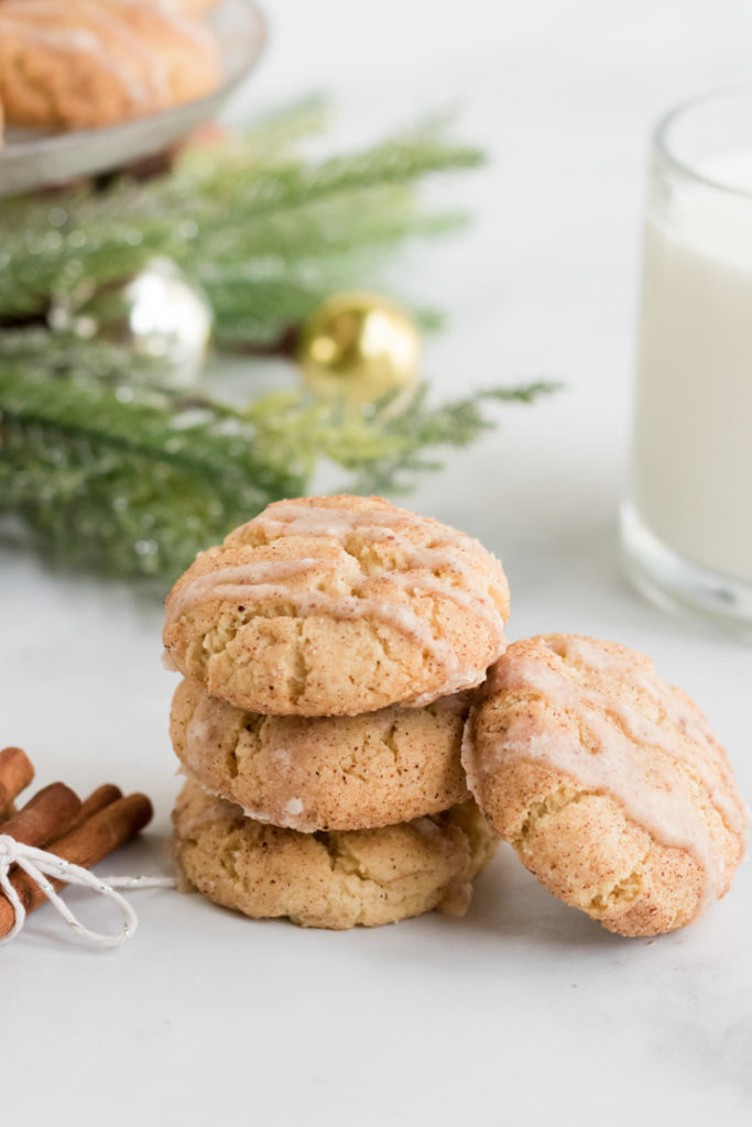 A stack of three egg nog cookies with a 4th cookie leaning up against it. A glass of milk is in the background