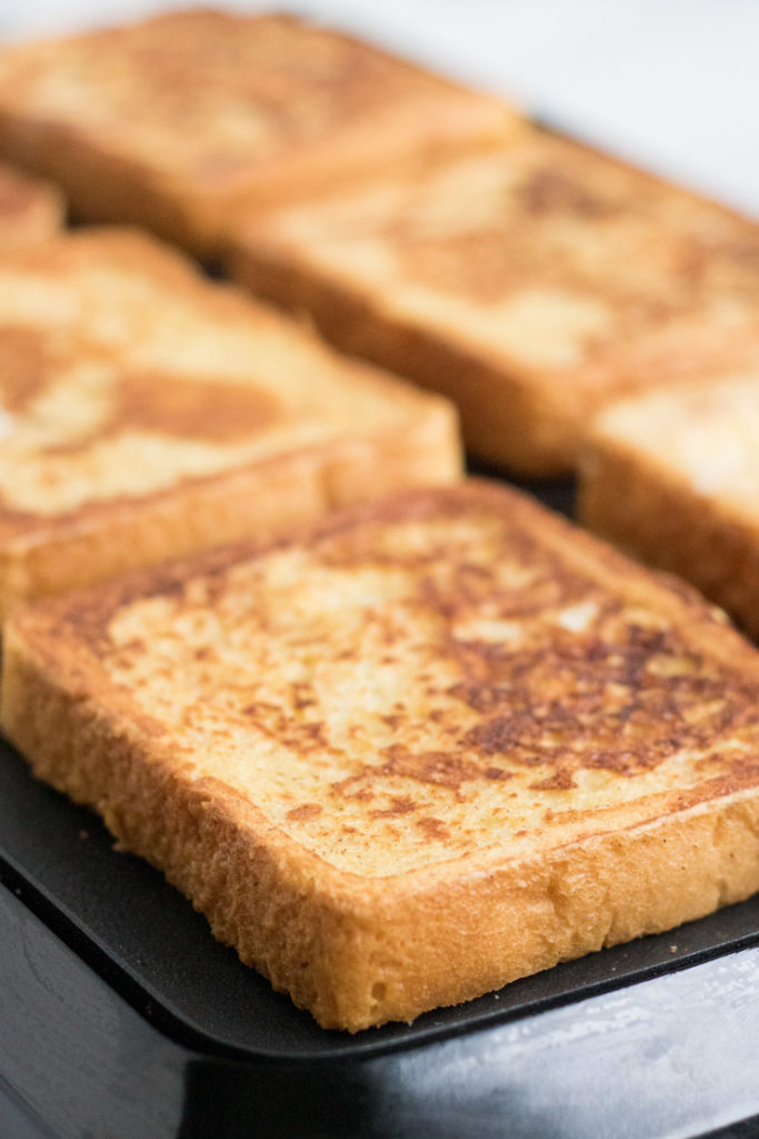 Egg Nog French Toast Recipe- egg nog french toast being cooked on an electric griddle. 