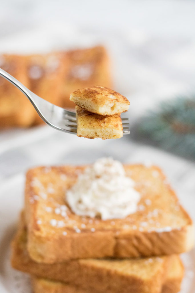 Egg Nog French Toast- a fork with a bite of french toast beind held up above the plate. 