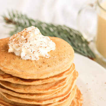 A big stack of egg nog pancakes with a bit of whipped cream on top.