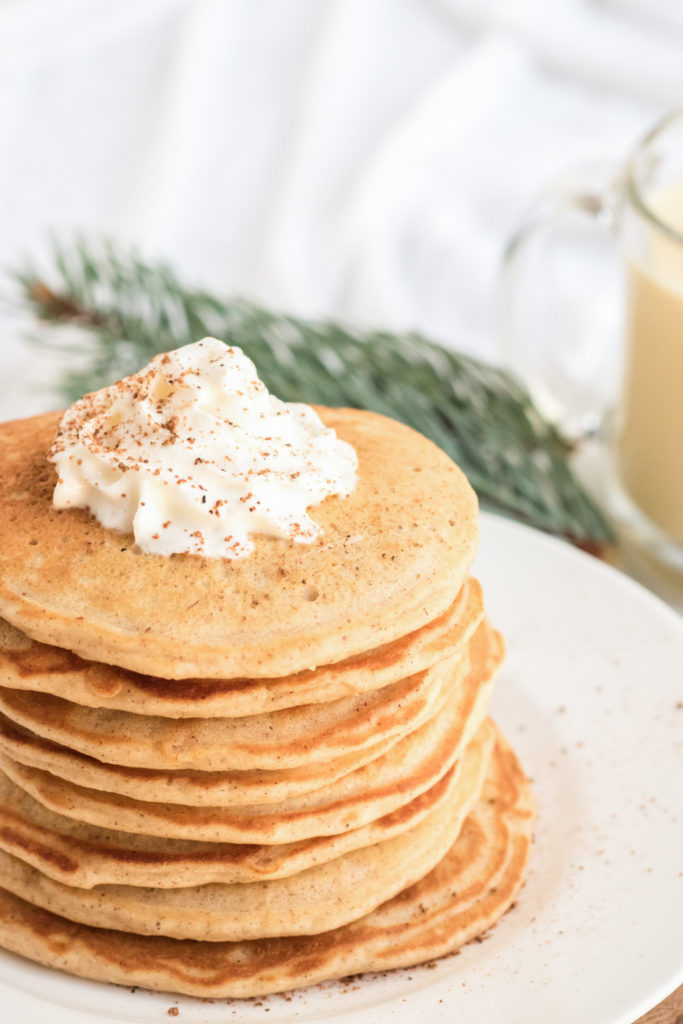 A stack of egg nog pancakes with whipped cream and nutmeg on top