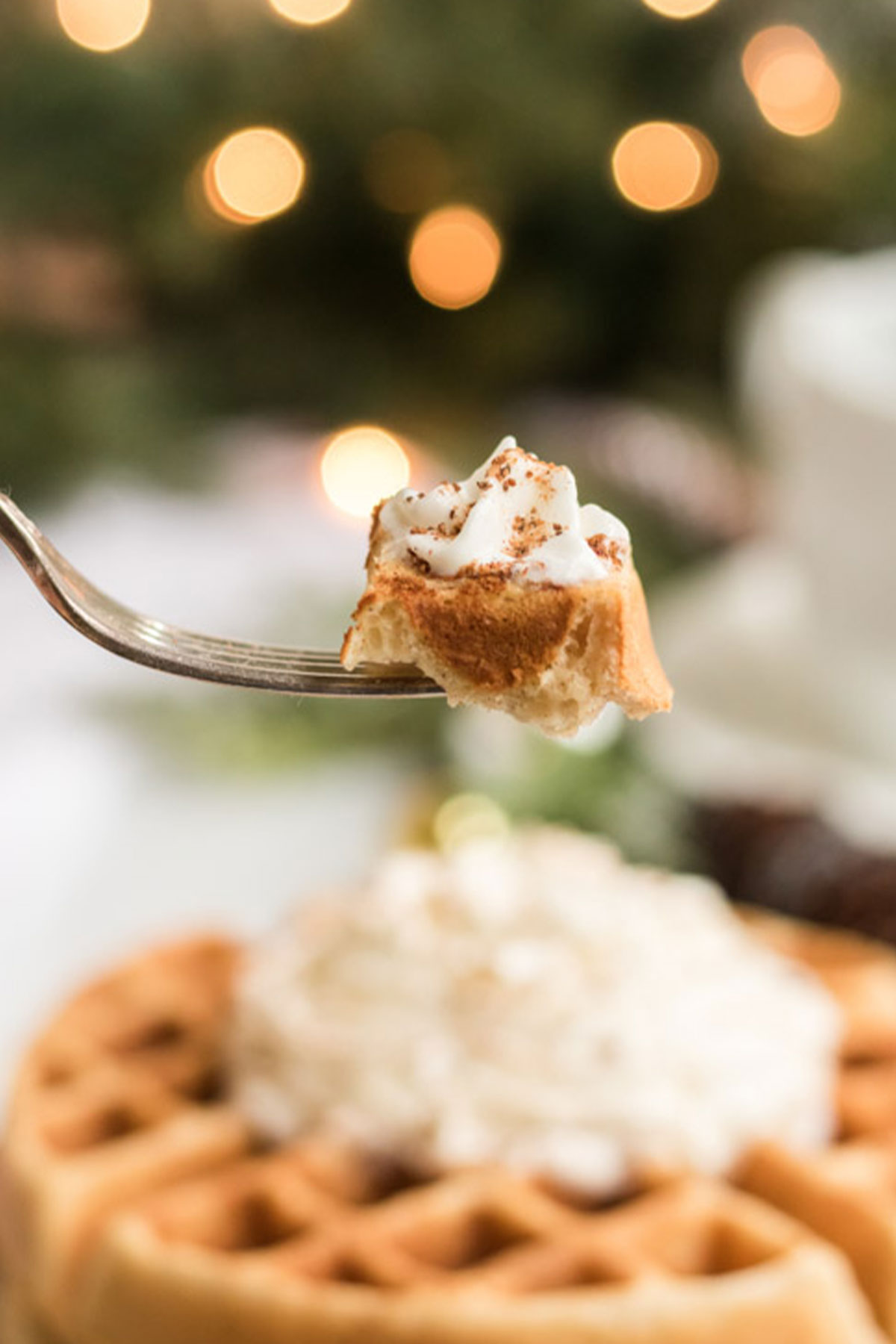 Bite of eggnog waffle on a fork with a stack in the background