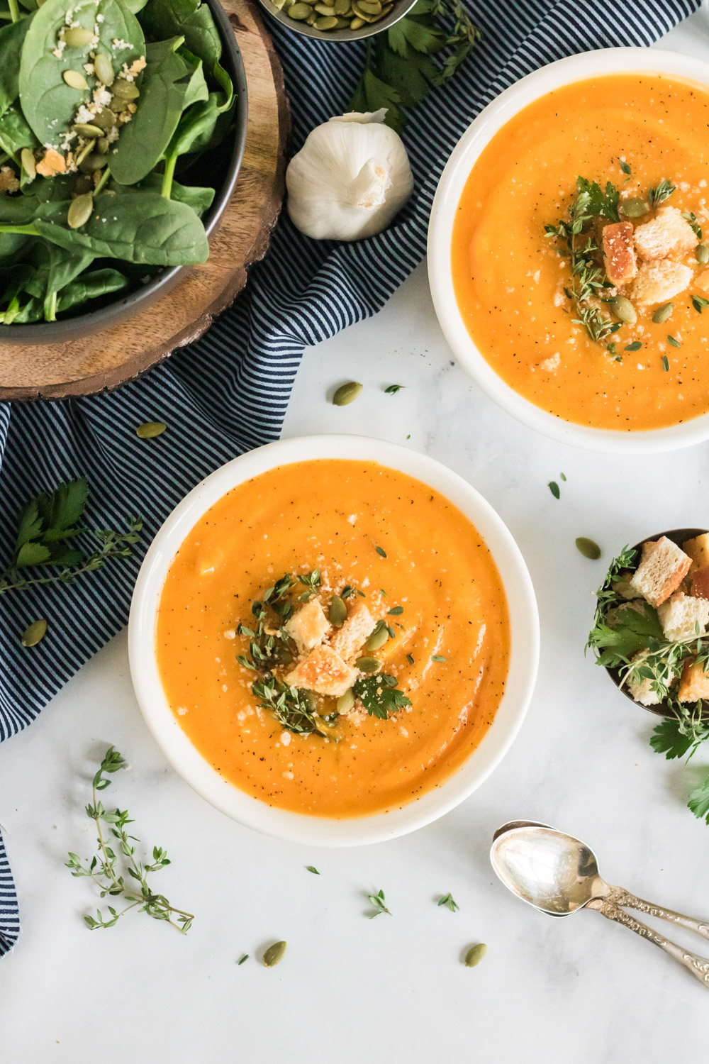 A bowl of butternut squash soup garnished with thyme, croutons and pumpkin seeds. 