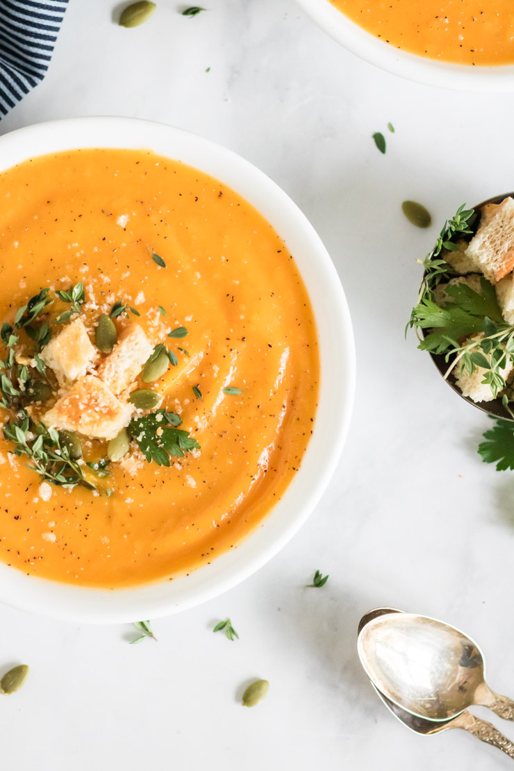 Half bowl shot of butternut squash soup. Topped with croutons, pepitas, thyme and parsley.