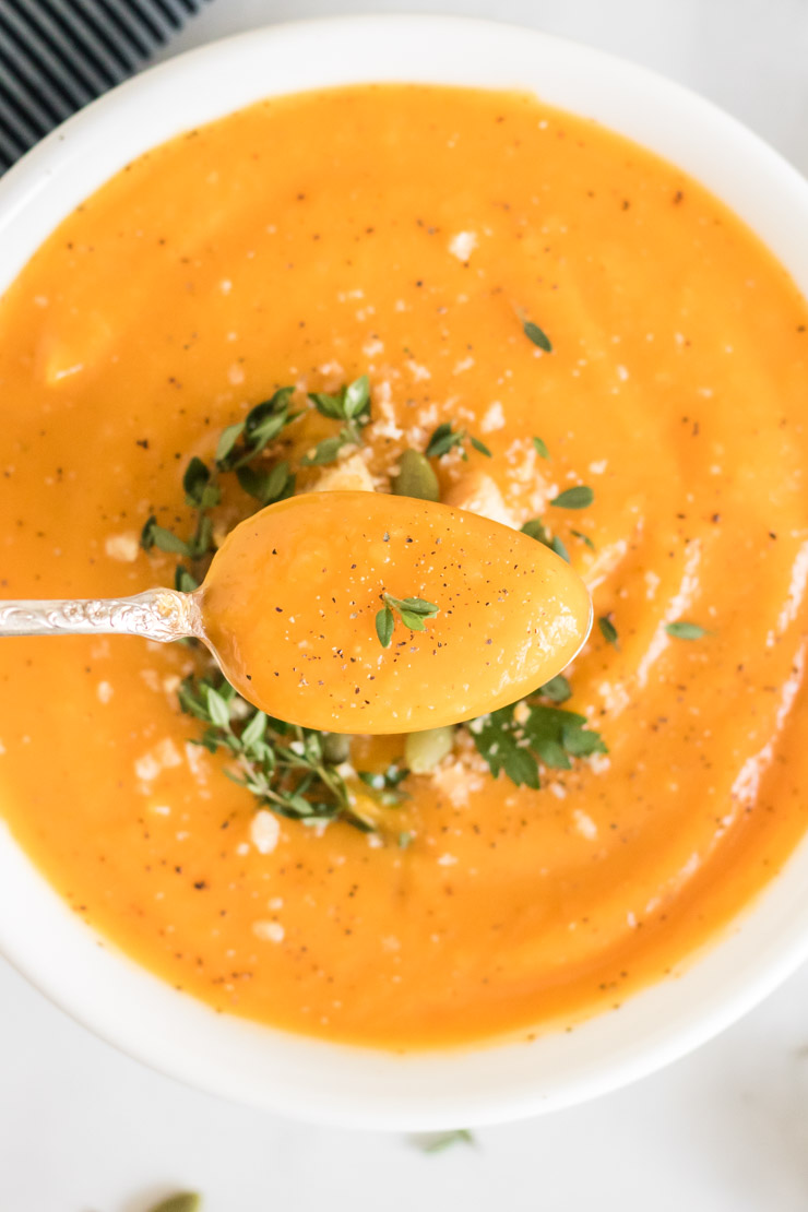 Butternut squash soup in a white bowl with a close up of a bite on a spoon.
