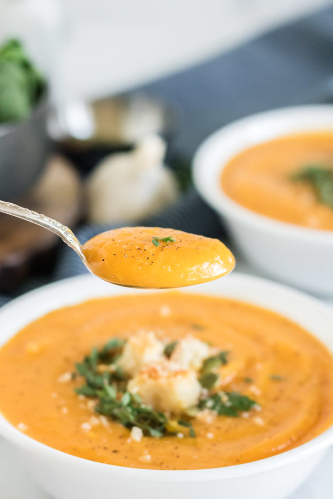 Butternut squash soup in a white bowl with a spoon over the bowl.
