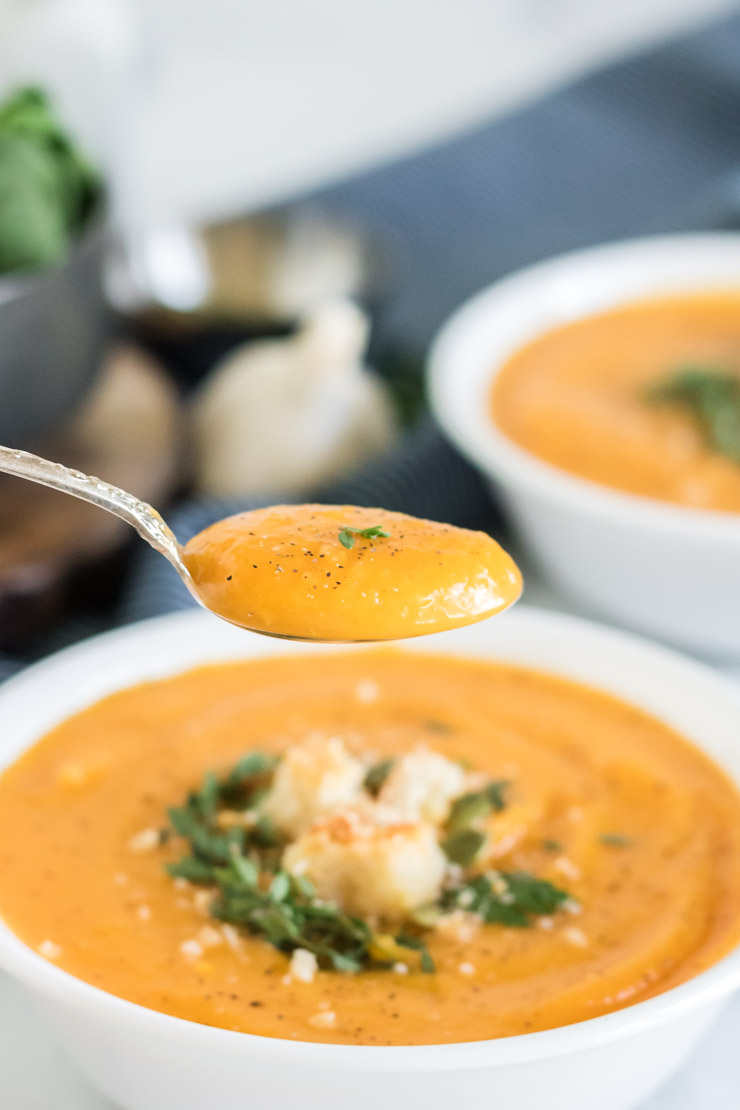 Butternut squash soup in a white bowl with a spoon over the bowl. 