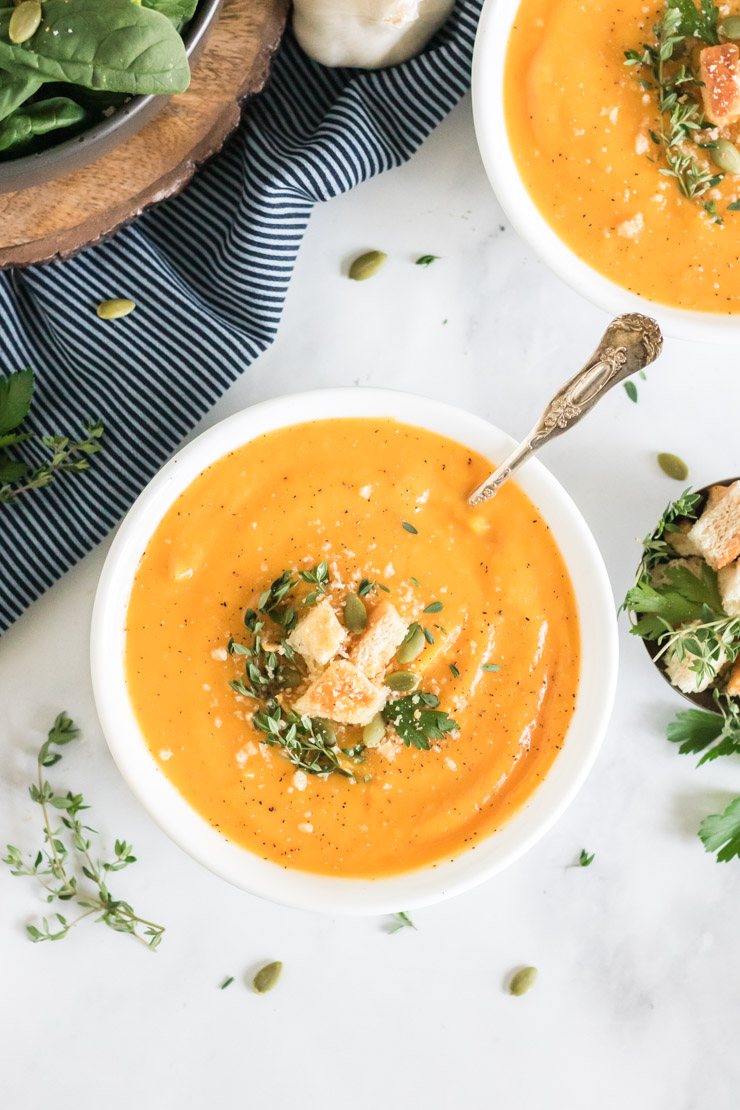 Vegan butternut squash soup with a spoon in it. It is garnished with croutons and fresh herbs. 