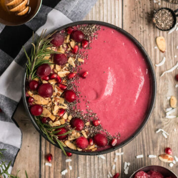 cranberry smoothie in a black bowl with cranberry, almond and chia garnishes.