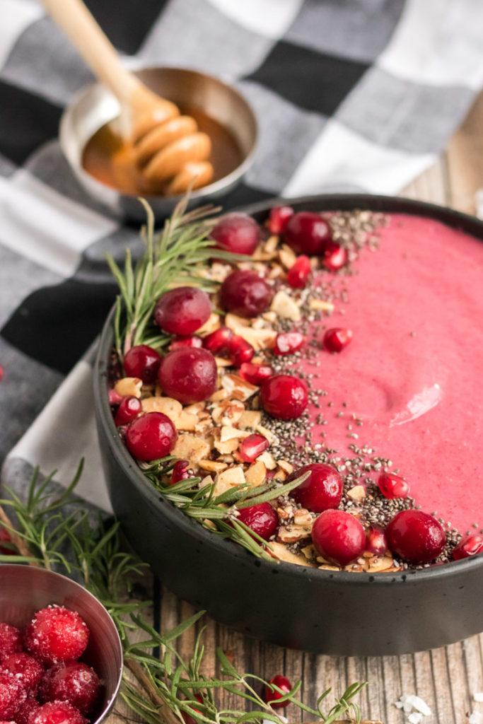 Image of half of a cranberry smoothie bowl with cranberries, almonds, chia seeds and rosemary. 