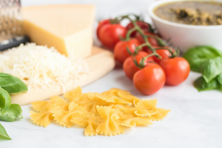 ingredients for chicken pesto pasta laying out. There is noodles, tomatoes, basil and parmesan cheese.