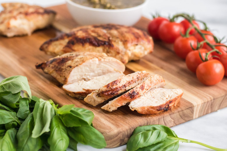 Grilled chicken breasts cut into slices with basil and tomatoes around it. 