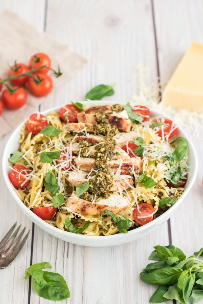 A 45 degree image of a pesto pasta salad in a white bowl on a wooden styling board. 