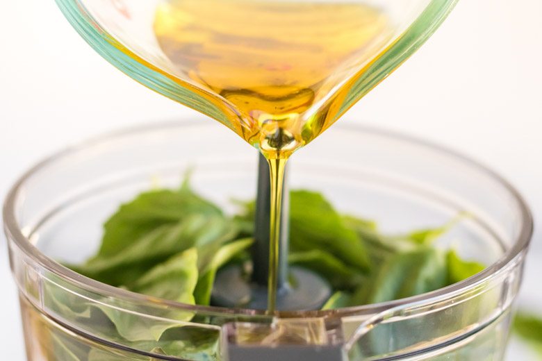 Olive oil being poured into a food processor to make nut free basil pesto