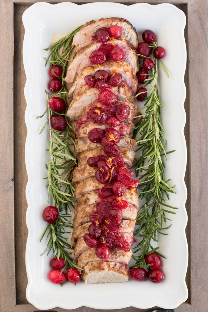 Overhead image of cranberry orange pork tenderloin with cranberries, orange zest and rosemary around it. 