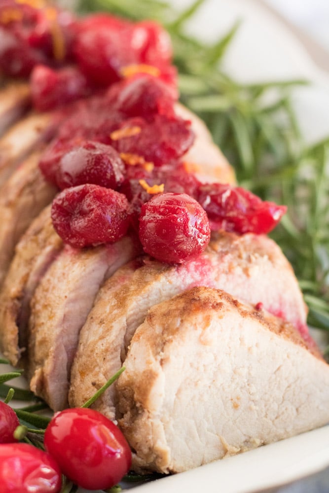 Close up image of pork with cranberries on top and rosemary along the sides. 