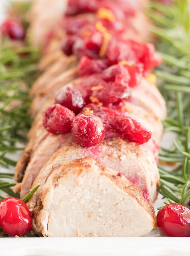 Pork Tenderloin slices in a row with cranberries on top and rosemary on the sides