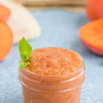 A small glass jar of persimmon butter with a sprig of mint.