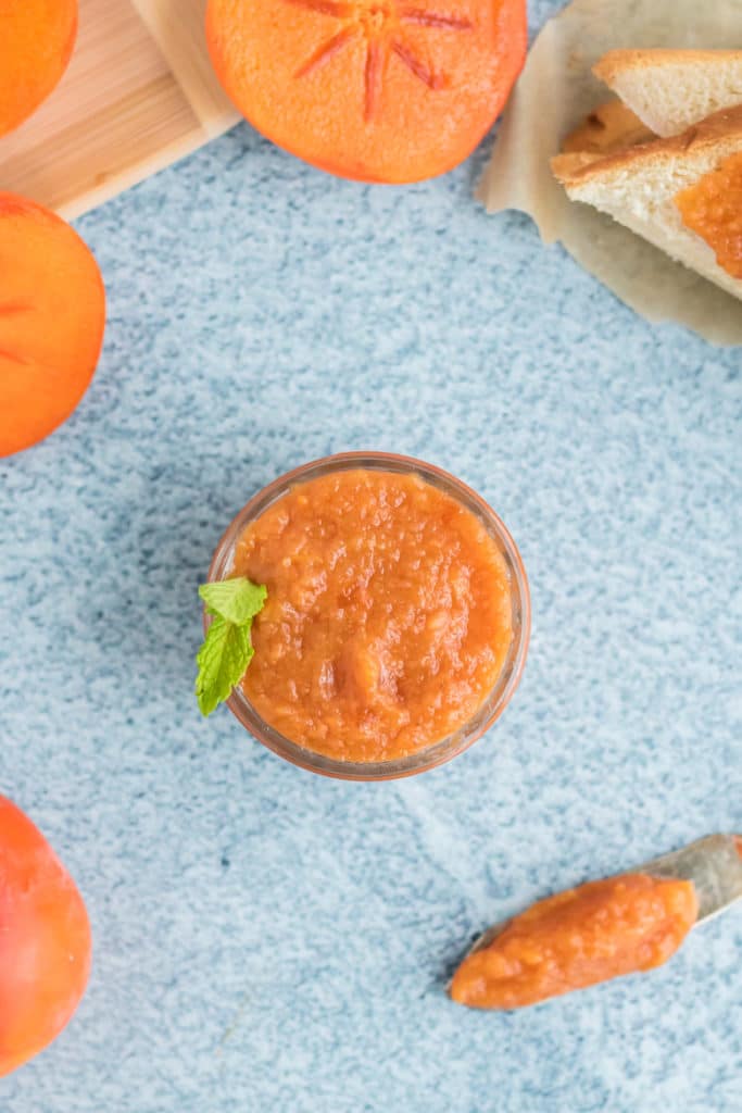 Overhead image of persimmon jam in a glass jar on a blue background. 