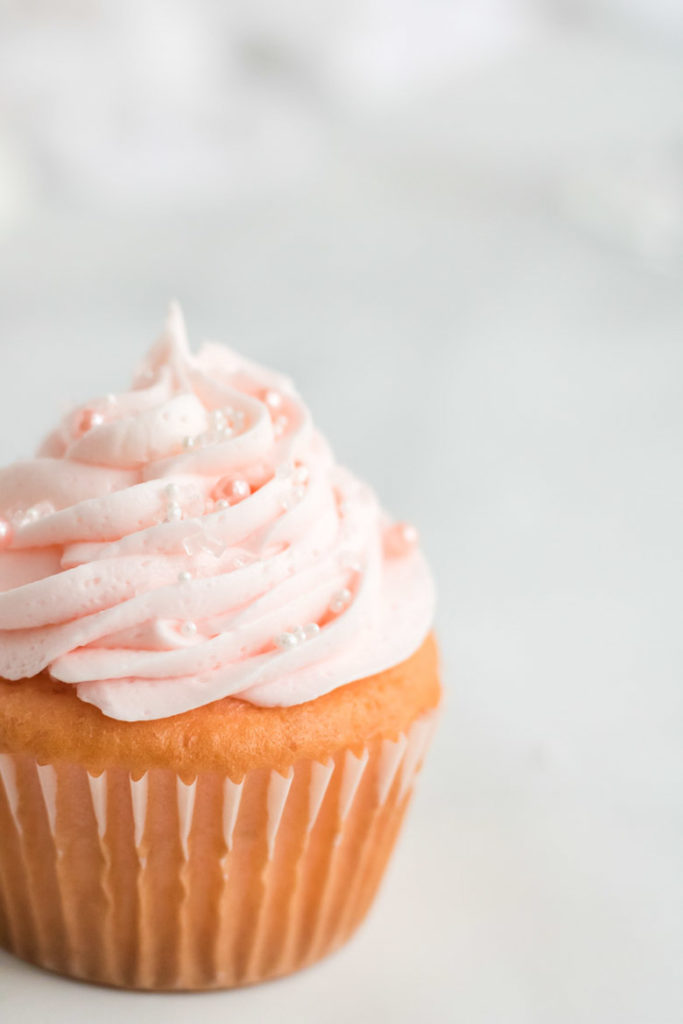 A close up of a pink champagne cupcake with white and pearl sprinkles. 