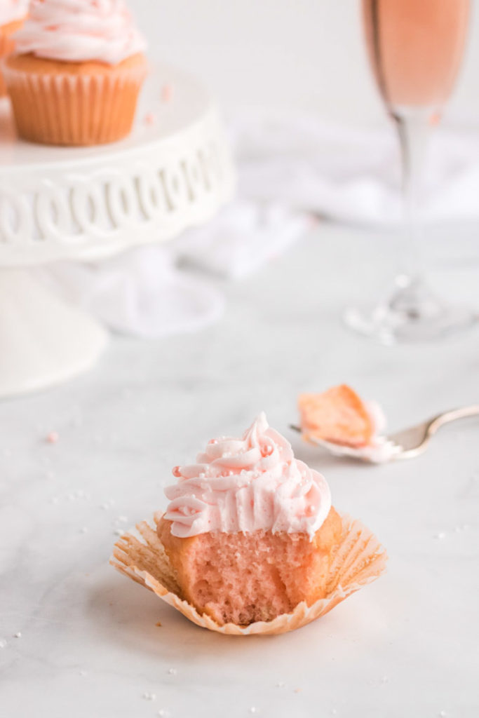 A pink champagne cupcake with a bite out of it and a fork behind it. 