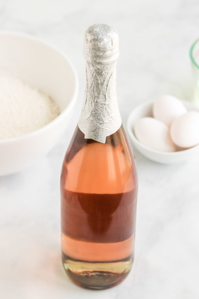 Ingredients for pink champagne cupcakes. A bottle of pink champagne with cupcake ingredients behind it. 