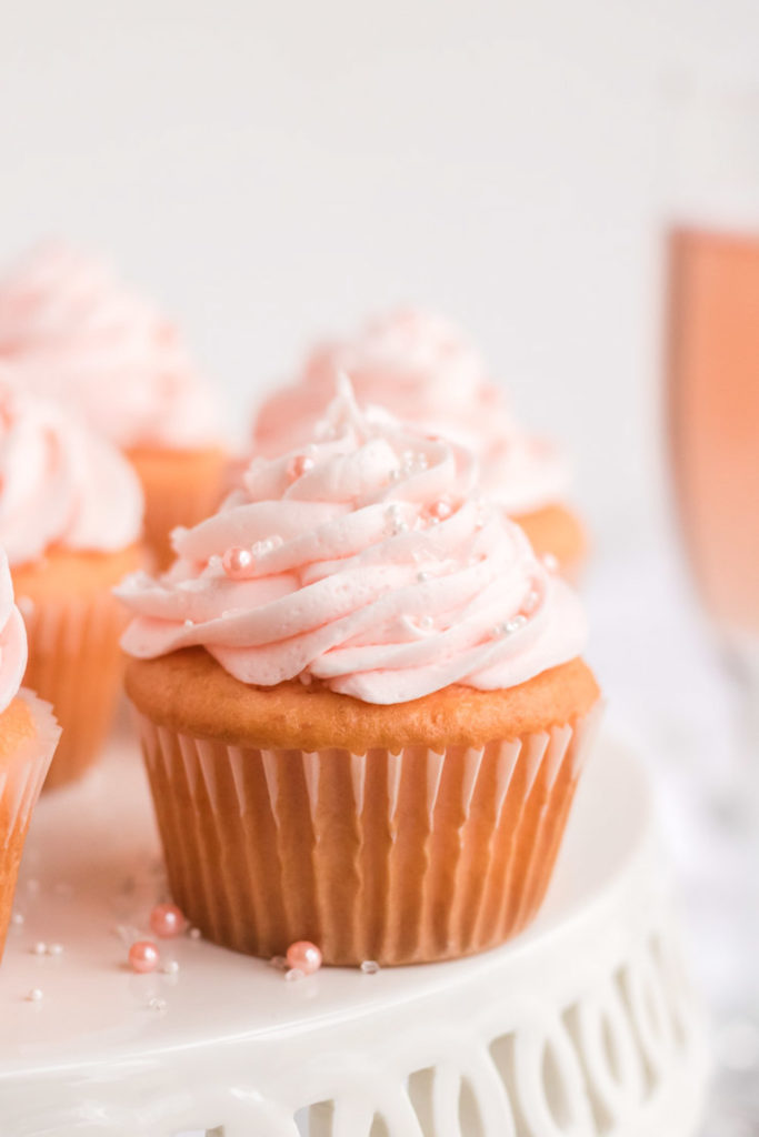 Pink Champagne Cupcake on a Cake stand with a glass of pink champagne behind it. 