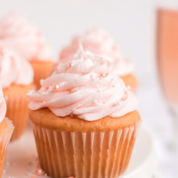 Pink champagne cupcake on a white cake stand with a glass of pink champagne behind it.