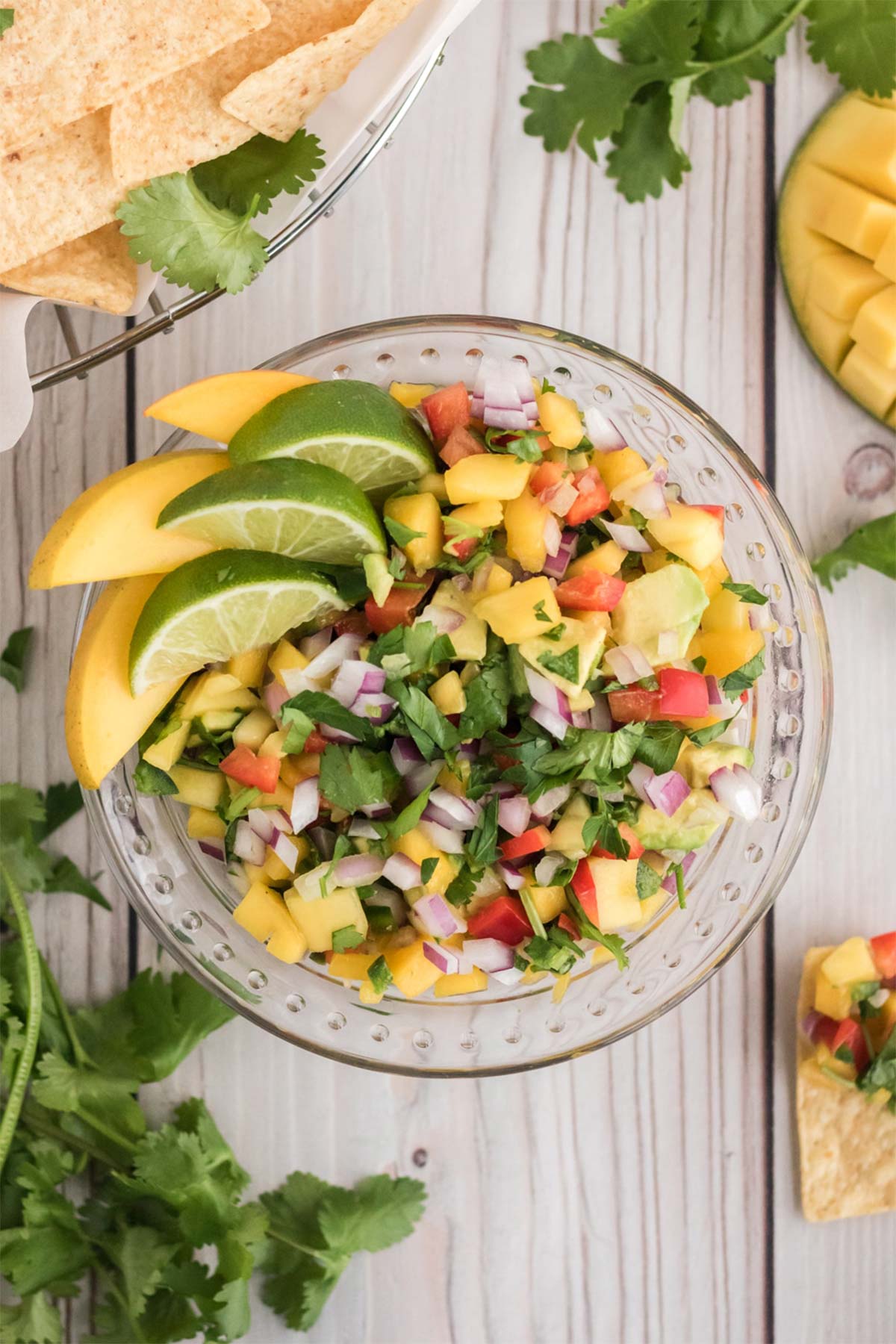 Overhead view of mango salsa garnished with mango wedges and lime wedges in a glass bowl.