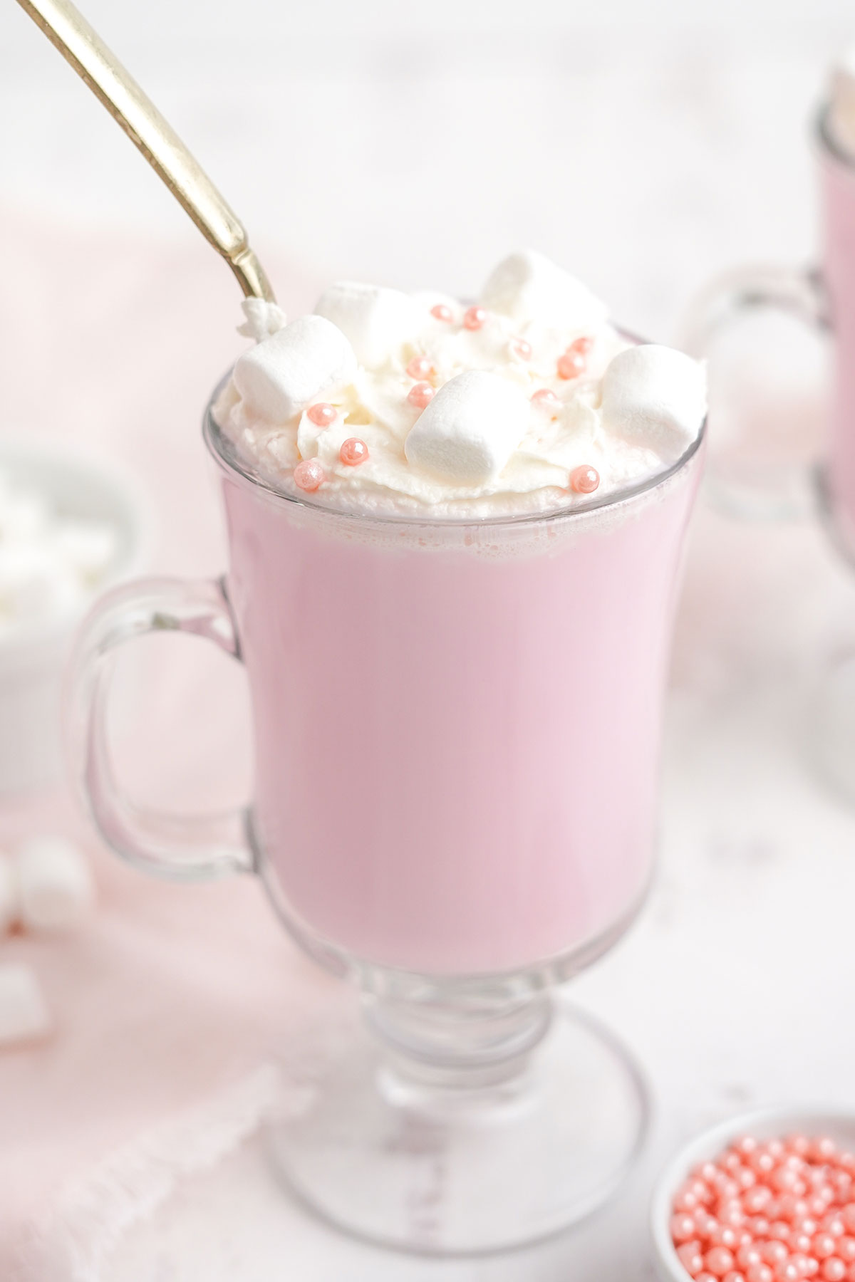 Close up of a mug of pink hot chocolate with whipped cream and pink pearl sprinkles.