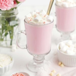 Two mugs of pink hot chocolate on the table with spoon in the glass.