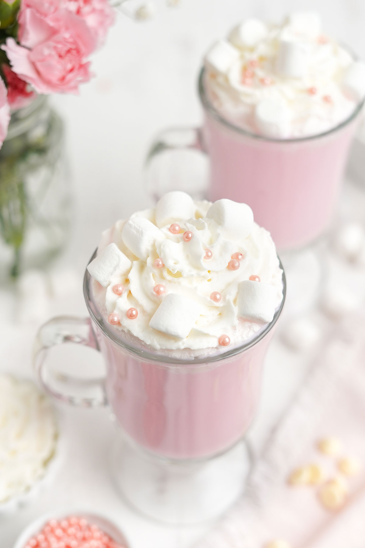View of two mugs of pink hot chocolate topped with whipped cream.