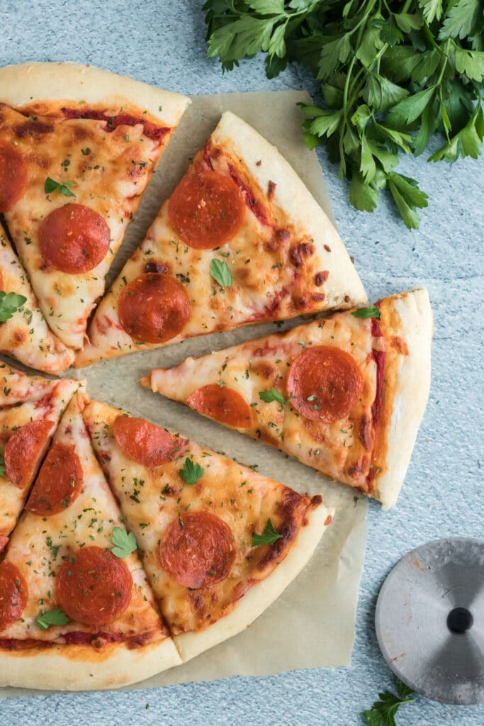 Homemade pepperoni pizza on parchment paper with parsley in the top corner. 