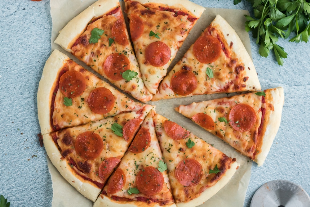 Overhead image of a pizza on parchment paper on a blue slate background.