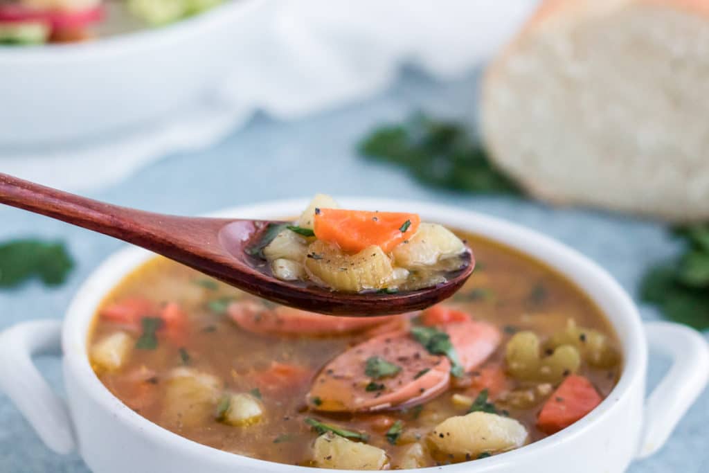 A spoonful of German Potato soup behind lifted from a white bowl. 
