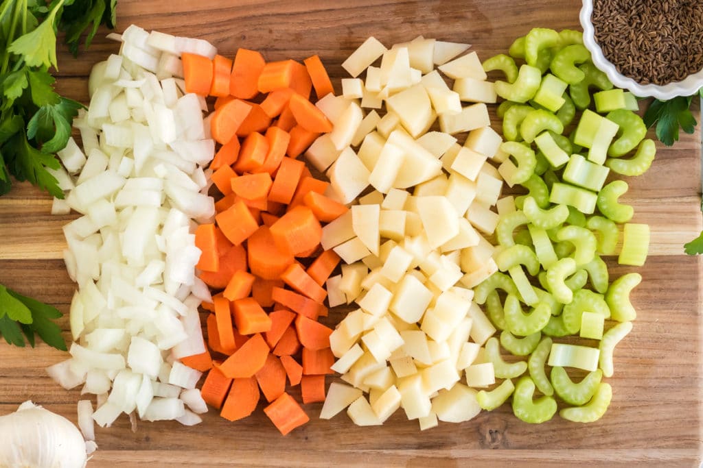 Ingredients for Kartoffelsuppe, or German soup. There are onions, carrots, potatoes, celery, parsley and caraway seeds lined up on a cutting board. 