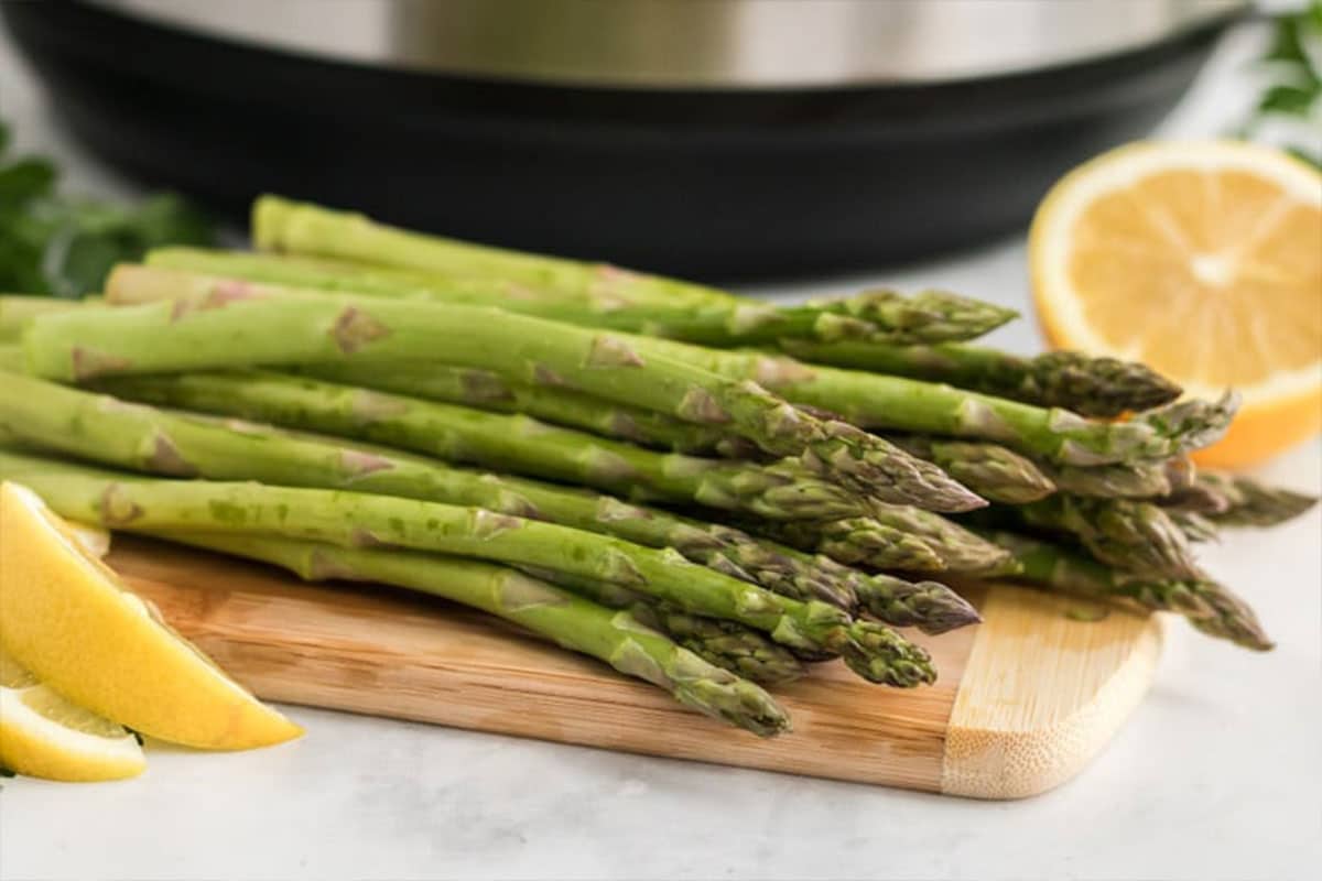 Fresh asparagus on a cooking board in front of an instant pot. 