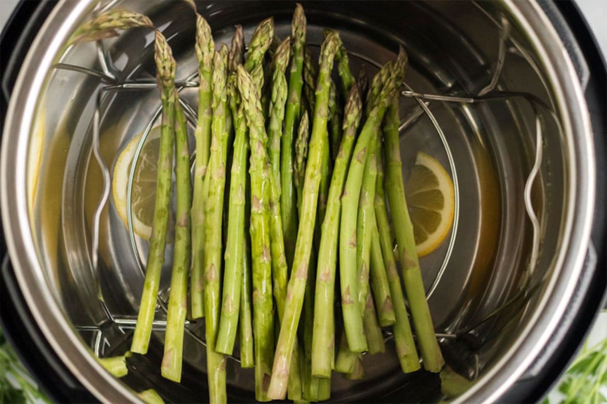 Asparagus in an instant pot being cooked on a steaming rack with lemon water. 