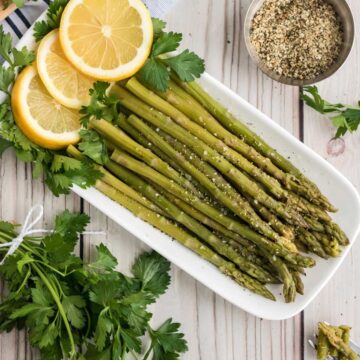 Instant Pot asparagus on a white plate with lemons and parsley.