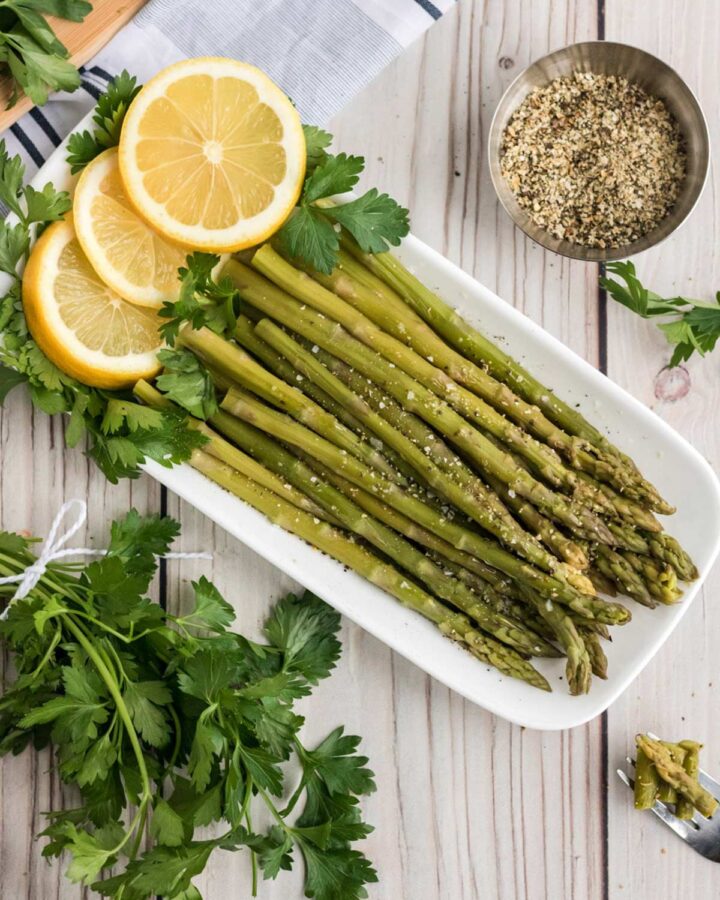 Instant Pot asparagus on a white plate with lemons and parsley.