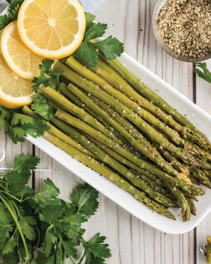 Instant pot asparagus on a white rectangle plate with fresh lemon slices.
